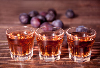Plum vodka or brandy with fresh plums on the wooden table.
