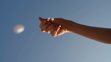 hand drops pearl beads on top of the camera. relaxing, naive, romantic, creative Slow motion video footage. Blue summer sky on the background. girly decorations homemade. Beautiful hobby time