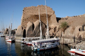 Wycieczkowe łodzie motorowe i żaglówki na rzece Nil w Asuanie przy skałach i pozostałościach...