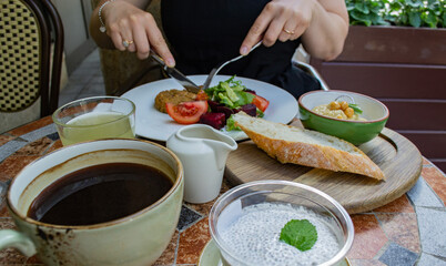 Someone outdoor is not eating vegetarian food: vegetable and beet salad and vegetable cutlet, lemonade, bowl of hummus and a piece of bread, cup of coffee and dessert: chia and coconut milk mousse