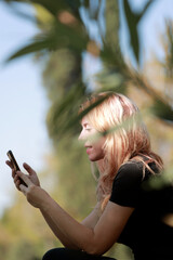 mujer de perfil sentada en un parque escribiendo en su teléfono móvil