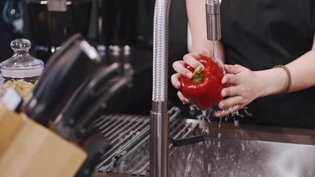 Fresh vegetables splashing in water before cooking. Wonan in a black apron.