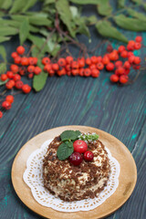 Sponge cake with butter cream. Decorated with cranberries and mint. Nearby are rowan branches with berries. Against the background of brushed pine boards.
