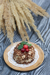 Sponge cake with butter cream. Decorated with cranberries and mint. Nearby is a bunch of dry grass with ears. Against the background of brushed pine boards.