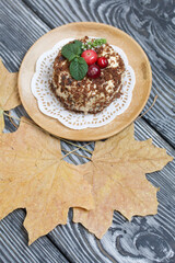 Sponge cake with butter cream. Decorated with cranberries and mint. Nearby are dried maple leaves. Against the background of brushed pine boards.