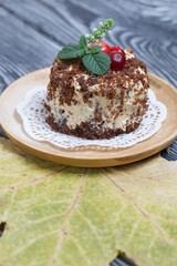 Sponge cake with butter cream. Decorated with cranberries and mint. Nearby are dried maple leaves. Against the background of brushed pine boards.