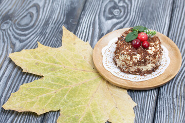 Sponge cake with butter cream. Decorated with cranberries and mint. Nearby are dried maple leaves. Against the background of brushed pine boards.