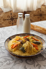 Vertical shot of Moroccan traditional beef and vegetables couscous served on a table with  spoon, glass, laban milk, water and bread with natural light and Morocco style decoration.