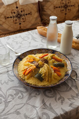 Vertical shot of Moroccan traditional beef and vegetables couscous served on a table with  spoon, glass, laban milk, water and bread with natural light and Morocco style decoration.