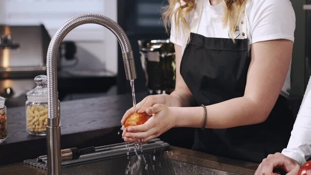 Fresh vegetables splashing in water before cooking. Wonan in a black apron.