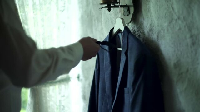 Kuchl / Austria - August 23 2019: Morning preparations of groom. Man&rsquo;s jacket and bow tie hangs on wooden hanger. Groom takes bow tie. White patterned tulle in the background. Slow. Man&rsquo;s suit details