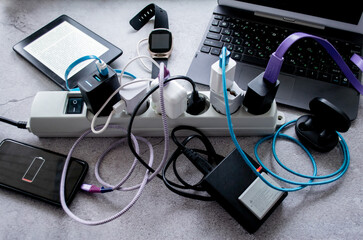 Many gadgets: smartphone, wireless headphones, laptop, smart watch, camera battery and e-book are charging on one power strip