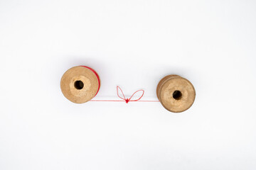 Top view of two wooden spools of thread. One is full, the other almost empty, connected by a single thread with a knot in the shape of a heart. Love and togetherness as a concept, without people