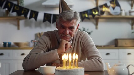 Deeply disappointed senior man sitting alone at kitchen table in front of cake with lit candles, celebrating birthday without relatives, suffering from loneliness, thinking of life. - Powered by Adobe