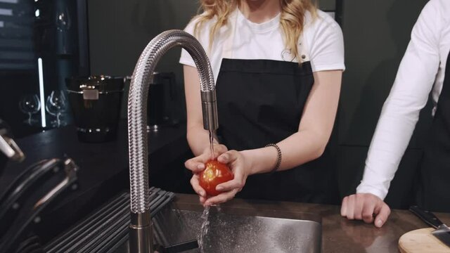 Fresh vegetables splashing in water before cooking. Wonan in a black apron.