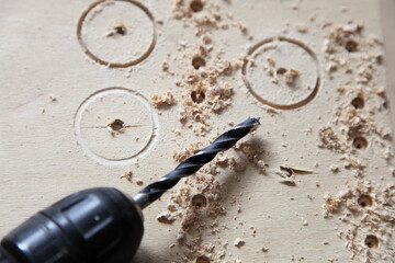 Spiral drill wood bit in electric drilling machine quick-release chuck close-up on wooden background with shavings, DIY drilling holes in the plywood