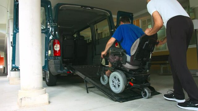 Man on wheelchair using accessible vehicle with ramp for transportation with driver helping.