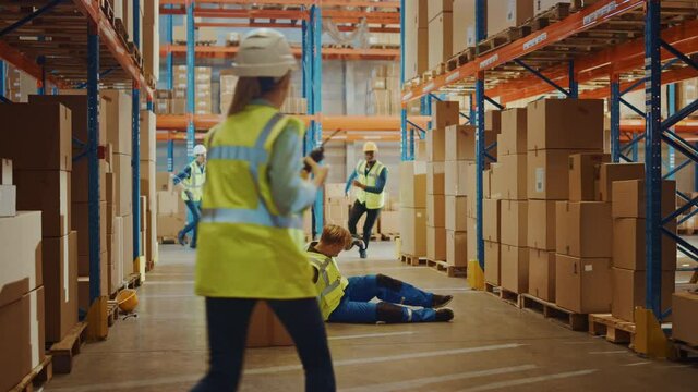 Warehouse Worker Has Work Related Accident Falls while Trying to Pick Up Cardboard Box from the Shelf. Colleagues Call for Help and Medical Assistance. Injury at Work. Slow Motion
