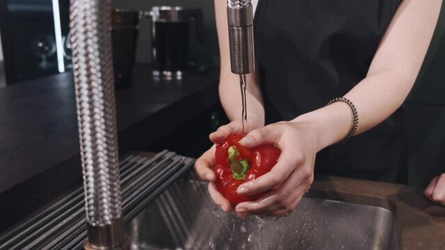 Fresh vegetables splashing in water before cooking. Wonan in a black apron.