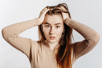 Beautiful young brunette girl in horror holding her head on an isolated white background. The woman is shocked by the bad news. Advertising space
