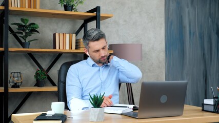 Tired man massages neck after using laptop computer long time, poor posture requiring treatment. Male student studying remotely online by video call conference web cam, distance education