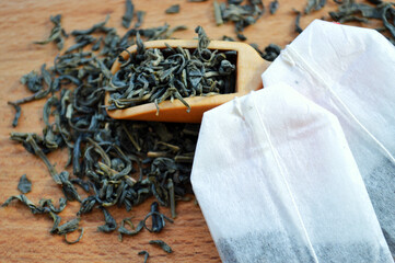 Tea bags and a wooden spoon lie on a heap of tea on a wooden background.
