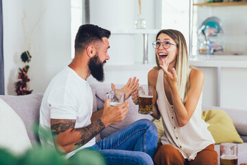 Young happy couple communicating while sitting on the sofa and drinking beer