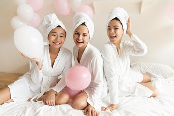 Smiling pretty young caucasian woman having fun with joyful beautiful asian girlfriends, wearing silk gowns and towels on heads, feeling relaxed after spa procedures, enjoying luxury hen party.