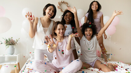 Happy young mixed race attractive girlfriends in nightwear having fun with colorful glitter...