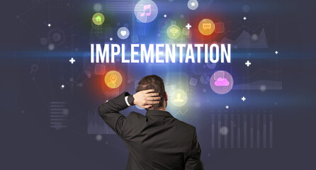 Rear view of a businessman with IMPLEMENTATION inscription, modern technology concept
