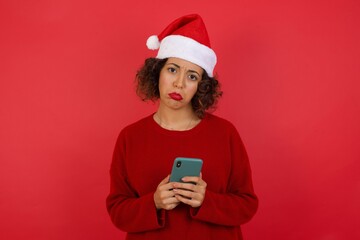 Portrait of a confused Caucasian woman holding mobile phone and shrugging shoulders and frowning face over isolated over gray background