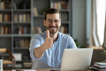 Portrait of smiling young Caucasian man in glasses sit at desk work on laptop recommend online...