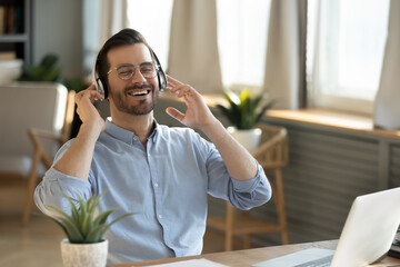 Overjoyed young Caucasian man in headphones relax at home workplace listen to music. Happy...