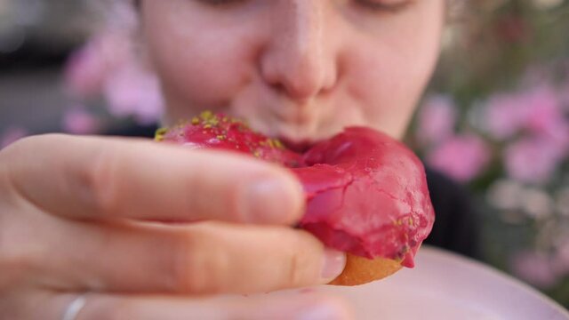 Close up of hungry female mouth biting vegan pink glazed doughnut and putting back on a pastel pink plate