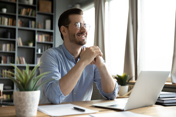Overjoyed young Caucasian male worker sit at desk at home office distracted from computer work...
