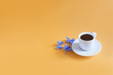 A cup of coffee and blue hydrangea flowers on a textured bright yellow-orange background. Copy space.