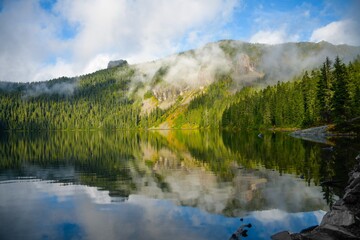 Mount rainier with clouds and a reflective lake in Washington