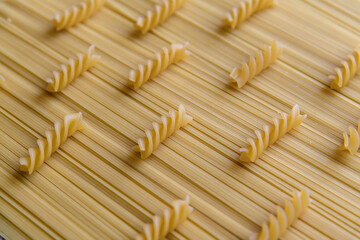 Raw uncooked fusilli pasta lies on raw spaghetti pasta. Abstract food background. Selective focus. Copy space for your text. Italian cuisine theme.