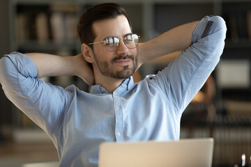 Happy calm young Caucasian male worker in glasses relax finishing computer work dreaming or visualizing. Smiling millennial man rest at home office workplace look in distance thinking or imagining.