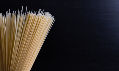 Abstract food background. Close up view of raw uncooked spaghetti pasta on black background. Copy space for your text. Italian food theme.