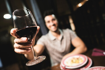 Handsome man doing toast with red wine in restaurant, looking at camera