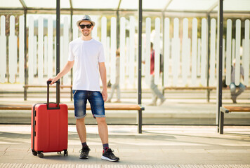 Fototapeta na wymiar Travelling guy with suitcase wearing smart style clothes waiting for transport.