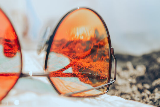 Sunglasses on a beach with reflection of summer beach with black sand, sun and sea.