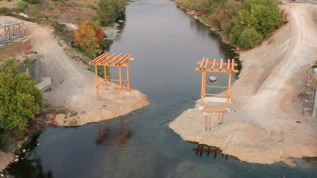 Bridge construction: metal scaffolding used as temporary support for the deck of a small pedestrian bridge. Pair of iron frames on the banks of a narrow river. 
