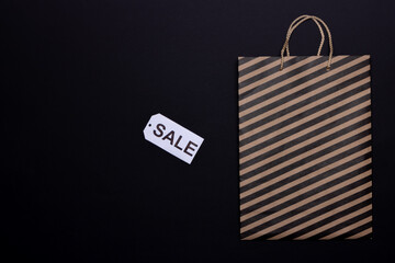 Top view of paper craft bag with black stripes and sale tag on black background. Black Friday concept. Copy space