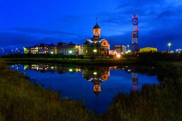 Fototapeta na wymiar Russian orthodox church in Yamburg - small town in north of Russia at night time with reflection in water.