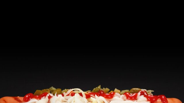 Hot dog with cream cheese, sauerkraut, jalapeno peppers and tomato sauce on a black background.