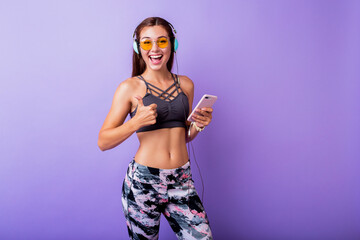 Exited sporty woman with  sincere  smiling posing in stylish active wear on studio. Using  smartphone   and listening   music.