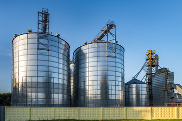 Obraz premium Modern Granary elevator with silver silos on agro-processing and manufacturing plant for processing drying cleaning and storage of agricultural products, flour, cereals and grain.