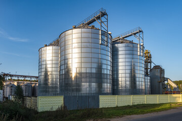 Obraz premium Modern Granary elevator with silver silos on agro-processing and manufacturing plant for processing drying cleaning and storage of agricultural products, flour, cereals and grain.